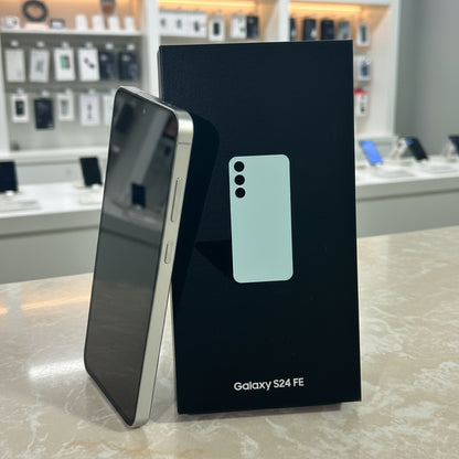Samsung Galaxy S24 FE phone next to its packaging on a light surface.